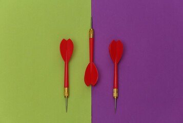 Three red plastic darts with metal tip on purple green background. Top view. Flat lay. Minimalism