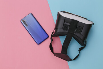 VR headset and smartphone on pink blue pastel background. Modern gadgets. Top view