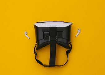 VR headset and wireless headphones on yellow background. Modern gadgets. Top view