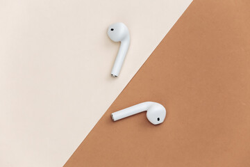 White wireless earphones on beige brown background. Top view. Flat lay