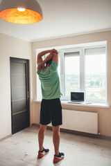 Fototapeta na wymiar back view photo of a caucasian man doing fitness at home using a laptop near the window