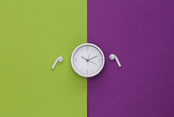 White clock and wireless earphones on a purple-green background. Top view