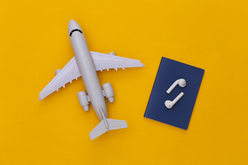 Passport and wireless earphones, air plane on a yellow background, travel concept. Top view