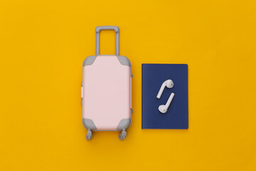 Mini travel luggage and wireless headphones, passport on yellow background. Top view