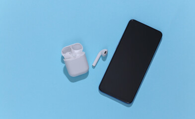 Smartphone and white true wireless bluetooth headphones or earbuds in charging case on bright blue...
