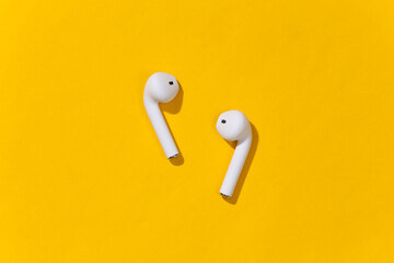 White true wireless bluetooth headphones or earbud on bright yellow background. Top view