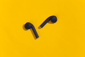 Classic blue color true wireless bluetooth headphones or earbuds on bright yellow background. Top view