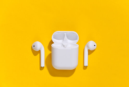 White true wireless bluetooth headphones or earbuds with charging case on yellow bright background. Top view