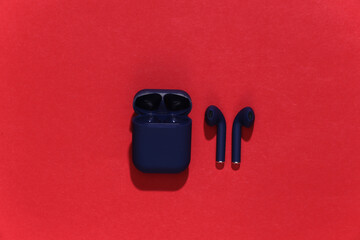 True wireless bluetooth headphones or earbuds with charging case on bright red background. Top view