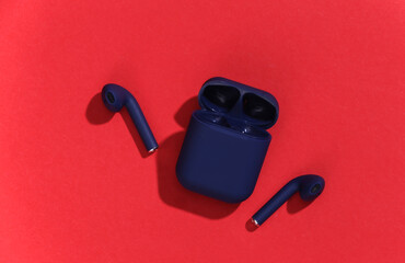 True wireless bluetooth headphones or earbuds with charging case on bright red background. Top view
