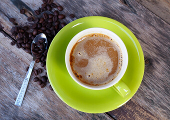 Coffee in green cup on old wooden table background, top view