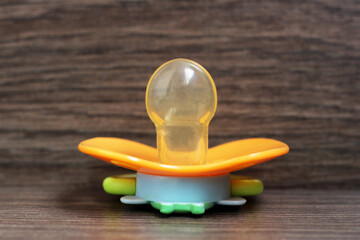 orange orthodontic pacifier on wooden background