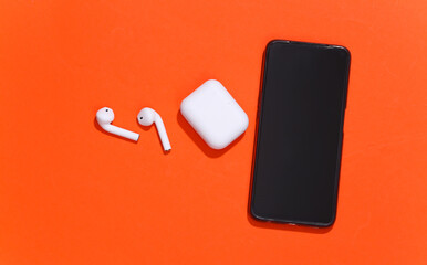 Smartphone and wireless bluetooth headphones or earbuds with charging case on bright orange...