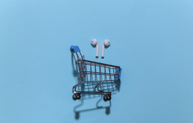 Mini shopping trolley with wireless bluetooth headphones on bright blue background. Top view