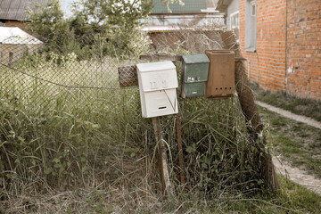 Vintage rustic mailboxes of different colors pinned on a fence.