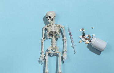 Skeleton and syringe, pills bottle on a blue bright background. Drug addiction. Top view