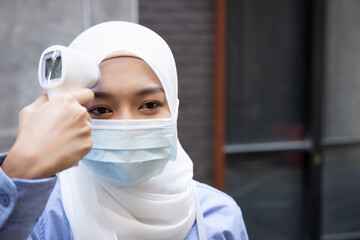 Fototapeta na wymiar Muslim woman shop keeper, small business owner do a business reopening preparation work by wearing proper face mask and thermal scan her fever before start working