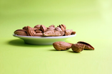 Almonds are not cleaned. In the center of a white plate are nuts. Three almond nuts lie separately on a yellow background. Food. A copy of the space. Quenching hunger. Protein. Nuts in shells. Nuts.