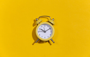 Yellow retro alarm clock on a yellow bright background. Top view. Minimalism