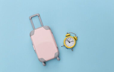 Mini travel luggage and alarm clock on blue pastel background. Time to travel. Top view