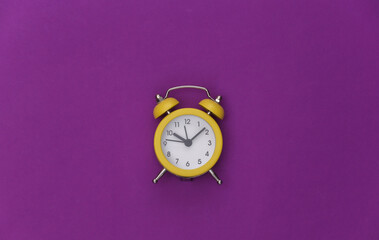 Yellow retro alarm clock on purple background. Top view. Minimalism