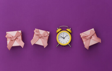 Mini alarm clock and gift boxes on a purple background. Top view. Minimalism
