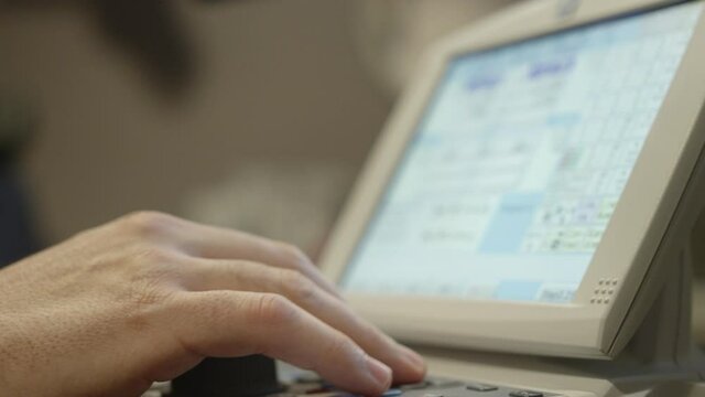 Middle aged male optometrist types on a small keypad and touch screen to produce an eyesight test for his patient.