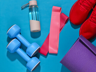 Flat lay fitness composition. Sports equipment on a bright blue background with deep shadow. Top...