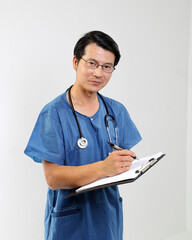 Young Asian male doctor wearing apron uniform tunic stethoscope write clipboard look at camera