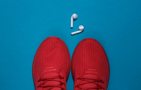 Red sports shoes and wireless headphones on a blue background. Sports accessories. Top view