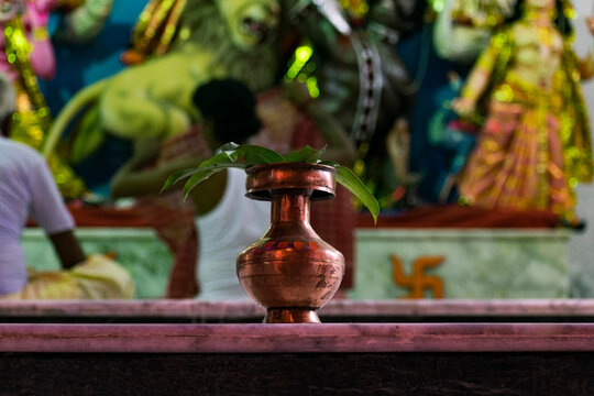 Red metallic lota with mango leaves on top in front of devi durga during durgapuja