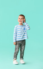 Cute little boy talking by phone on color background