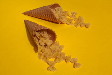 Ice cream waffle cones with pasta bows on yellow bright background