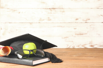 Graduation hat, book, apple and diploma on table