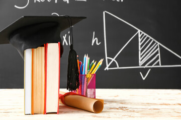 Graduation hat, books, stationery and diploma on table in classroom