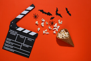 Clapper board, Ice cream waffle cones with decorative bats and spiders, popcorn on orange bright background. Top view. Scary movie. Flat lay halloween composition
