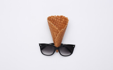 Ice cream waffle cone and sunglasses on white background, top view. Flat lay summer composition