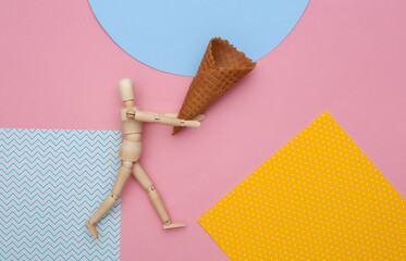 Wooden puppet holding Ice cream waffle cone on colored background. Top view. Flat lay