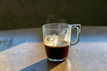 Unfinished cup of coffee on the old wooden table under the rays of the morning sun