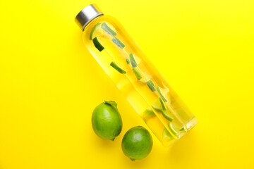 Fresh green limes and bottle of infused water on color background