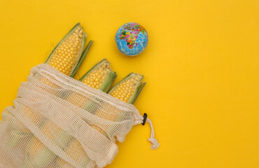 Eco cotton bag with corn swings and globe on yellow background. Save planet. Top view. Flat lay