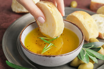 Woman dipping bread into bowl of tasty olive, closeup