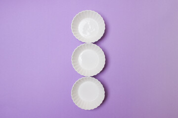 three empty white plate on purple colored paper background