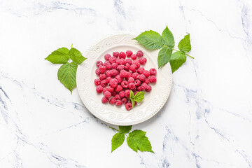 Plate with ripe raspberries on white background