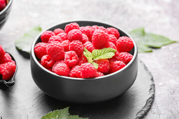 Bowl with ripe raspberries on grey background