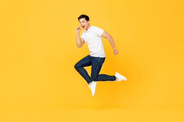 Fototapeta na wymiar Happy excited young Asian man jumping isolated on yellow studio background