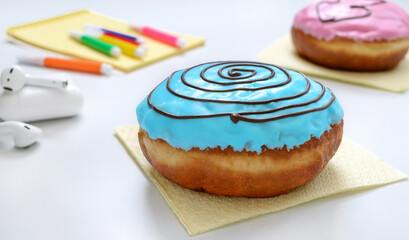 Berliner donut with blue frosting on a white office desk and materials for creativity. Snack dessert at the workplace, lunch break.