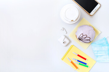 Berliner donut, coffee, headphones, medical mask and materials for creativity on a white office desk. Snack dessert at the workplace, lunch break. Copy space