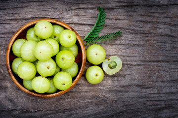 gooseberry fruits ( Amla ) in wooden bowl with green leaf isolated on wood table background. Top view. Flatlay.
