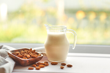 Almond milk in glass with almonds in wooden bowl on a white wooden table